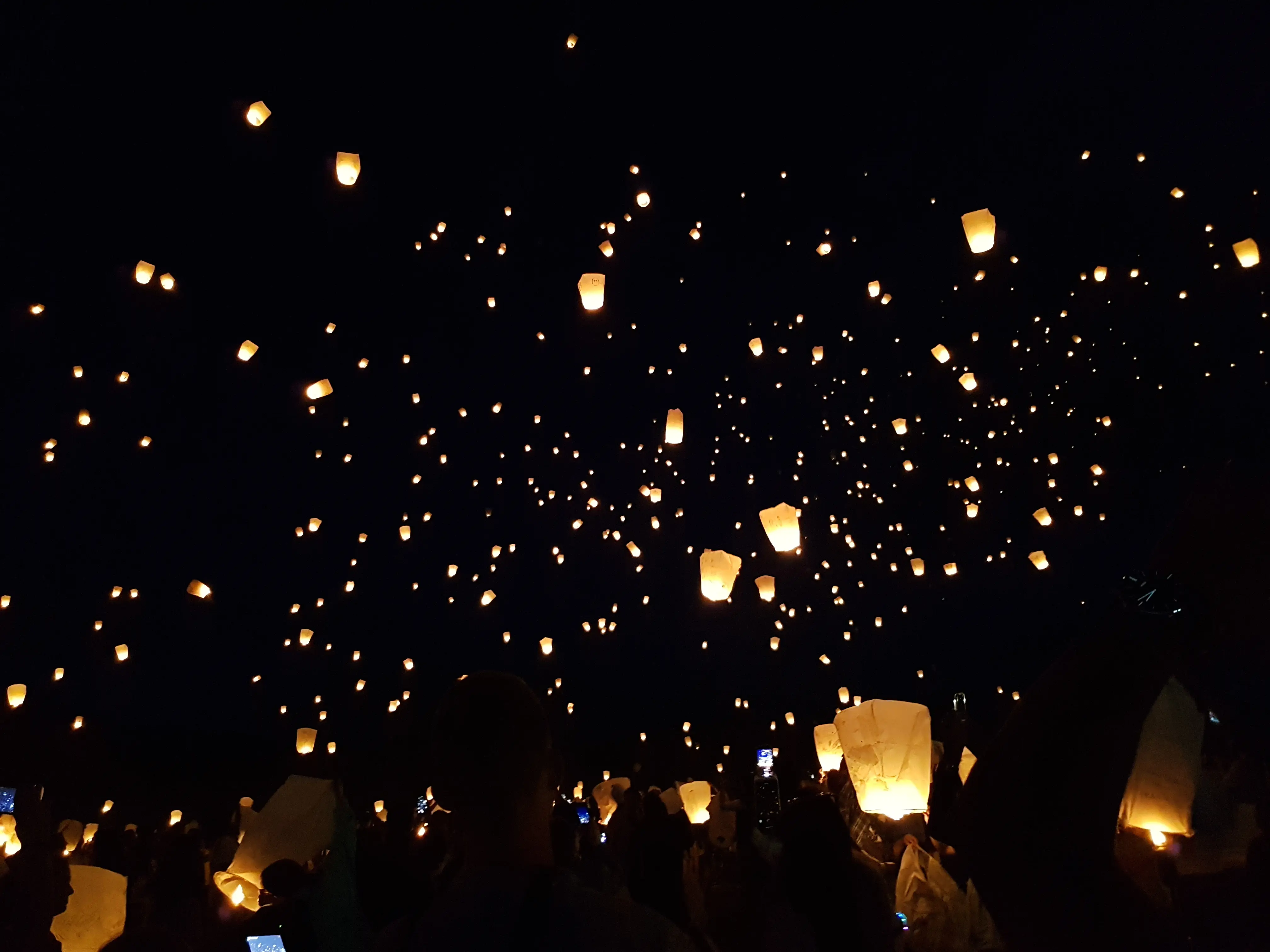 Sky lanterns rising into the night over a crowd